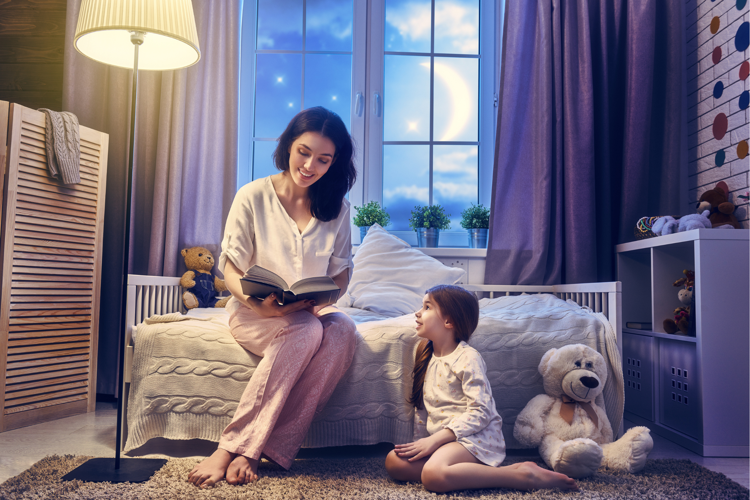 A mother reading her daughter a book lit by a bed lamp | The Best Smart Light Bulbs